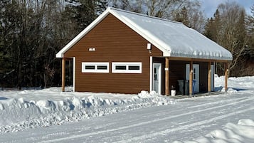 A wooden cabin with a snow-covered roof, a garage, and a covered porch area.