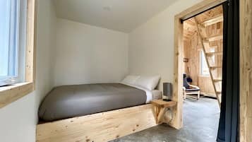 Une chambre à coucher comprenant un lit, une table de chevet, une chaise et une échelle en bois menant à un niveau supérieur.