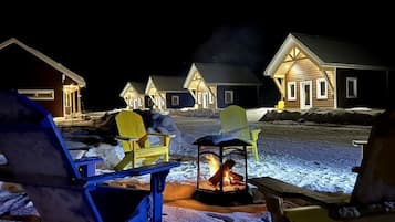 Un espace extérieur enneigé comprenant plusieurs cabanes en bois, un foyer et des sièges d’extérieur.