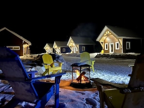 A snow-covered outdoor area with several wooden cabins, a fire pit, and outdoor seating.