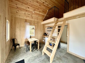 A wooden interior with a desk, chairs, a ladder, and a staircase.