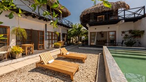 A resort with a pool, wooden lounge chairs, and thatched-roof buildings.