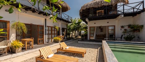 A resort with a pool, wooden lounge chairs, and thatched-roof buildings.