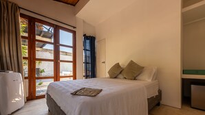 A bedroom with a bed, a window, a door, and a small kitchenette.