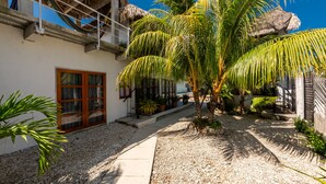 A courtyard with palm trees, a thatched-roof building, and a pathway.
