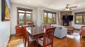 A spacious living area with a dining table, wooden chairs, a gray sofa, and a fireplace. - Private Hot Tub, Walk to Main St, Close to Ski Resorts, Incredible Views (Firsco)