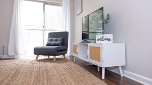 Un salón moderno con un sillón gris, un mueble de televisión blanco y un letrero que dice 'welcome'.
