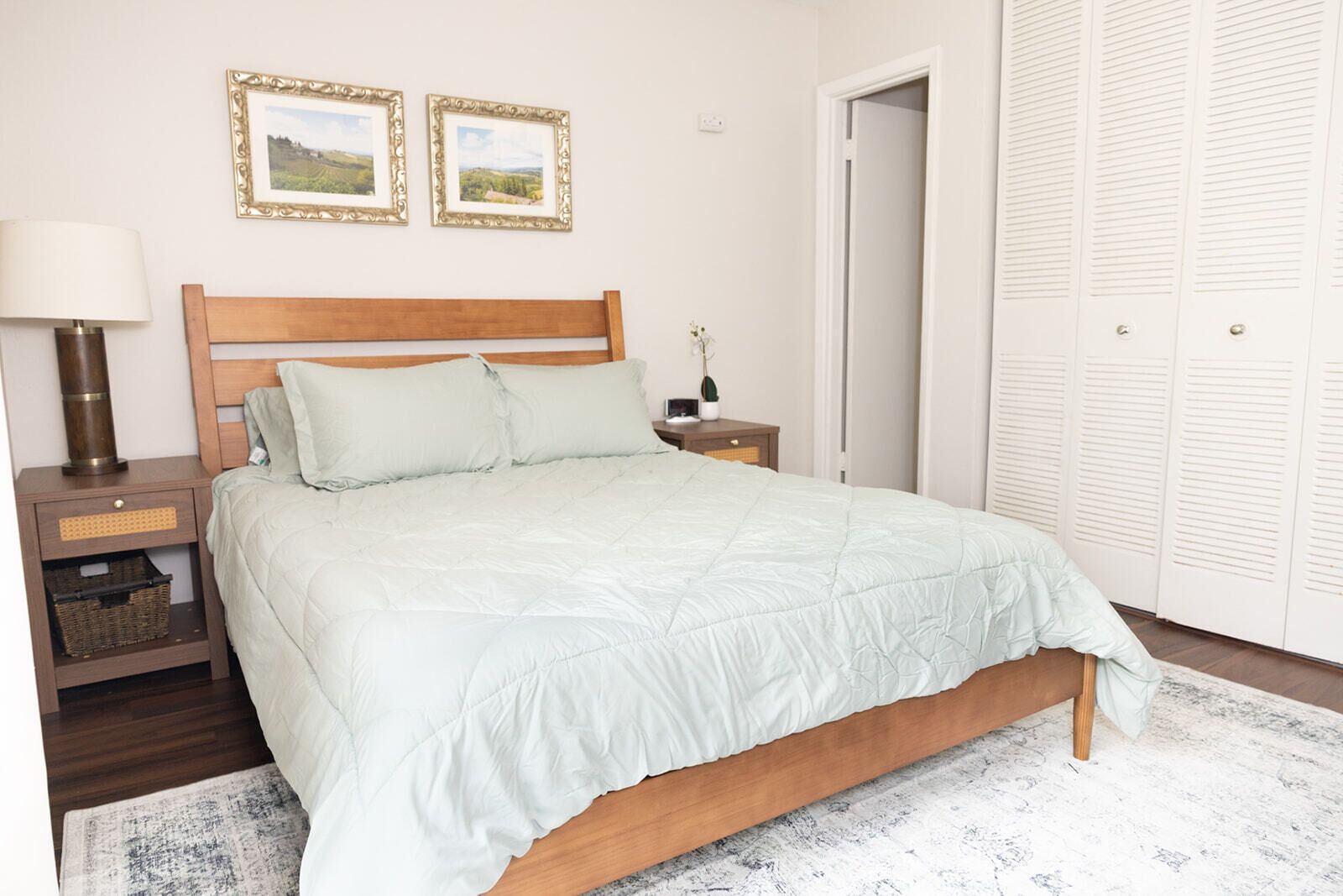 A bedroom with a wooden bed, a nightstand, a lamp, and a wall with two framed pictures.