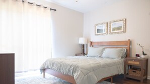 Un dormitorio con cama, mesita de noche, lámpara y dos cuadros en la pared.