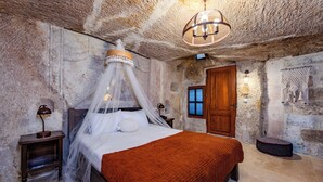 A bedroom with a bed under a canopy, a wooden door, and a stone wall. - Emars Cave Cappadocia (Ürgüp)