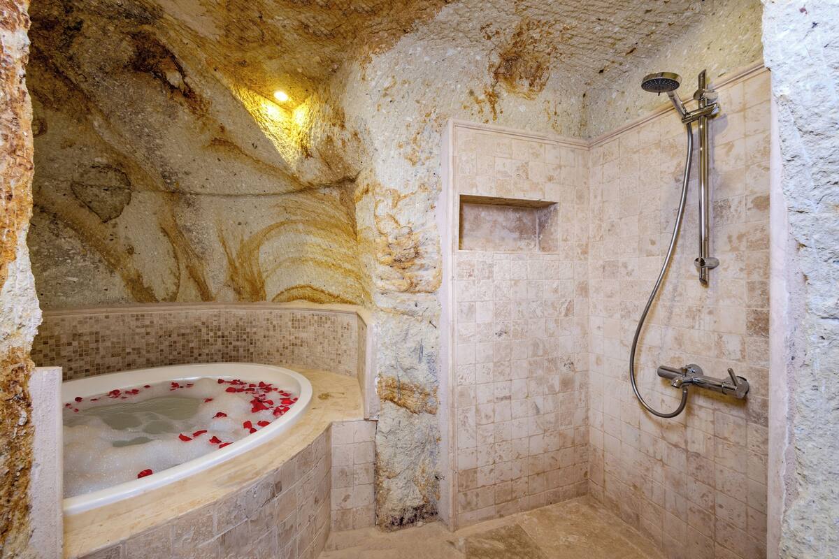 A bathroom with a stone wall, a bathtub with rose petals, and a shower with a handheld showerhead.
