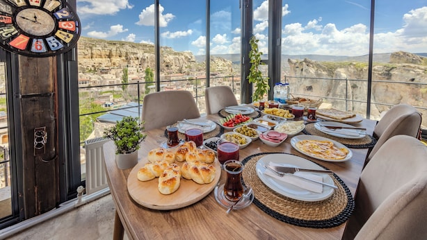 A dining table set with various dishes, a clock, and a view of a mountainous landscape. - Emars Cave Cappadocia (Ürgüp)