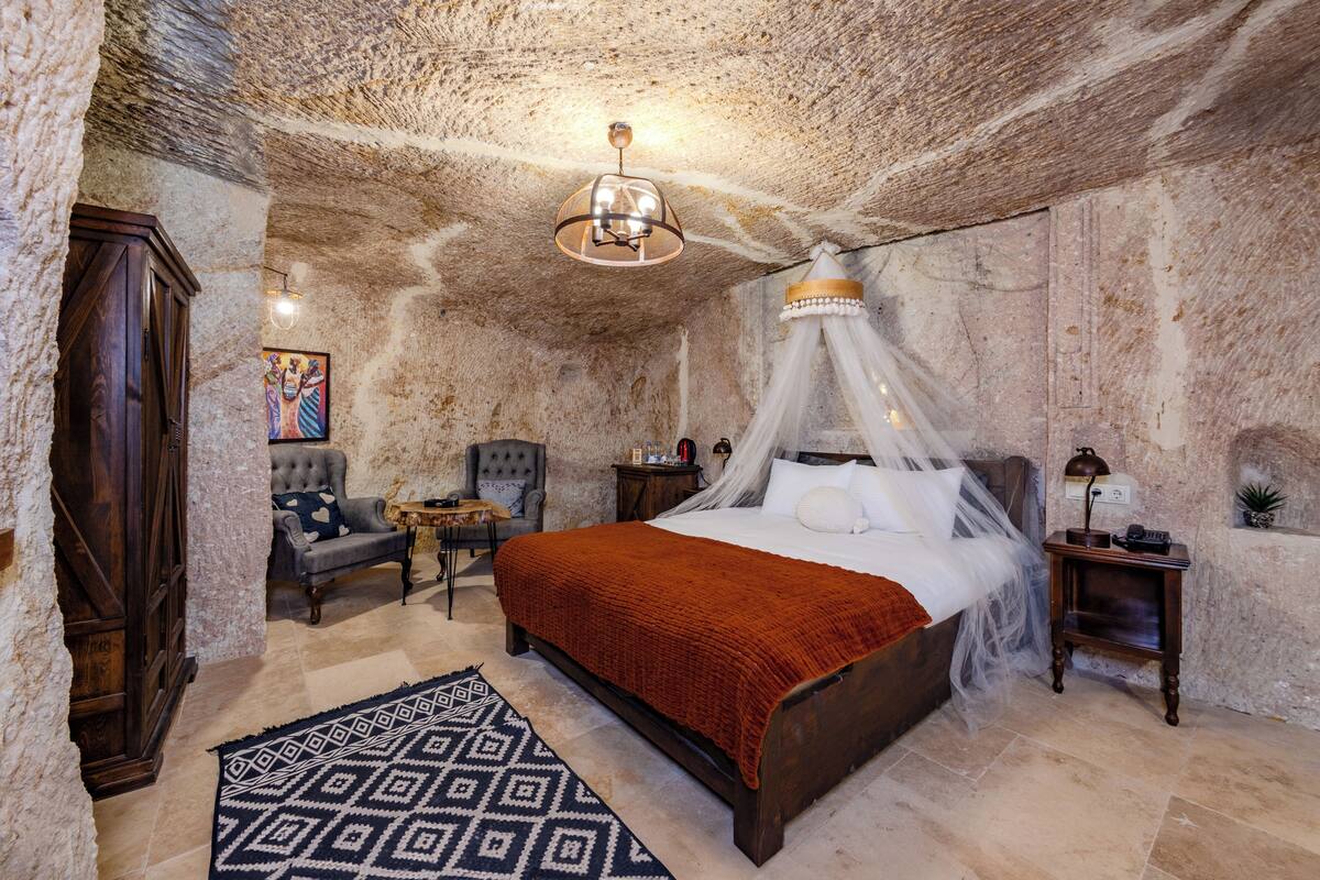 A bedroom with a four-poster bed, a nightstand, a chair, and a rug.