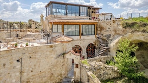 A stone building with a modern glass extension, outdoor seating, and a staircase leading to an upper level. - Emars Cave Cappadocia (Ürgüp)