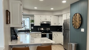 A modern kitchen with white cabinets, a large island with two brown bar stools, stainless steel appliances, and a wooden clock on the wall. - Lakeside Getaway on Lake Madison. Hot tub with a view of the lake! (Wentworth)