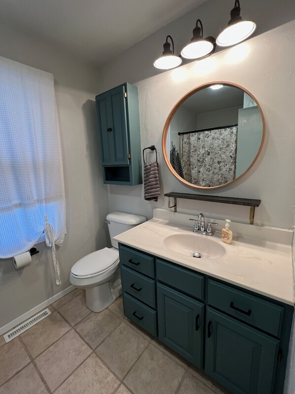 Un baño con inodoro, lavabo y armario. Hay un espejo sobre el lavabo y una cortina de ducha con estampado floral.