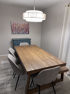 Un comedor con una mesa de madera, sillas tapizadas en gris, un armario azul, una lámpara colgante y un cuadro floral en la pared.