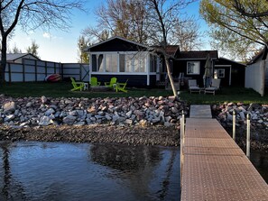 Una casa con patio trasero que incluye un estanque, un muelle de madera y sillas Adirondack verdes.