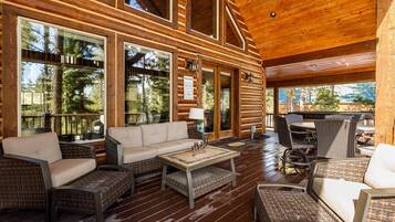 A spacious outdoor area with a wooden deck, wicker furniture, and large windows offering views of the surrounding forest.
