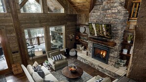 Een gezellig chaletinterieur met een stenen openhaard, houten balken en een groot raam met uitzicht op een terras.