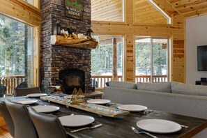 A cozy lodge interior with a stone fireplace, wooden beams, and a dining area set for a meal. - Aspen Glow! Brand New Hot Tub! (Duck Creek Village)