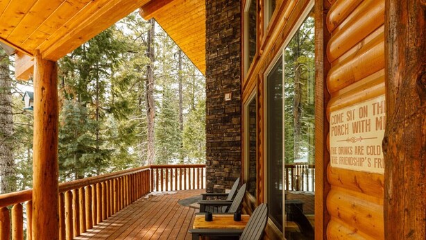 Terraza de madera con muro de piedra y puerta de cristal, con vista a un bosque.