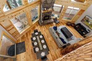A cozy cabin interior with a stone fireplace, wooden floors, and large windows. - Aspen Glow! Brand New Hot Tub! (Duck Creek Village)