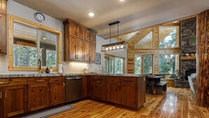 Una cocina amplia con armarios de madera, lavavajillas integrado y ventanas grandes con vistas al bosque circundante.