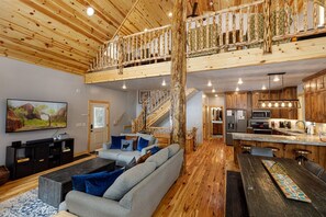 A spacious living area with a large sofa, a television, and a wooden staircase leading to an upper level.