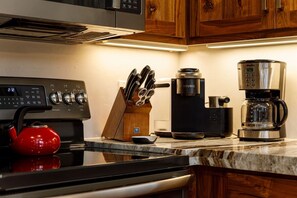 A kitchen with a black stove, a red kettle, a coffee maker, and a knife block.