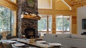 Interior acogedor de una cabaña con chimenea de piedra, vigas de madera y un comedor listo para una comida.