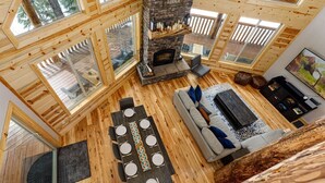 Un interior de cabaña acogedor con chimenea de piedra, piso de madera y ventanas amplias.
