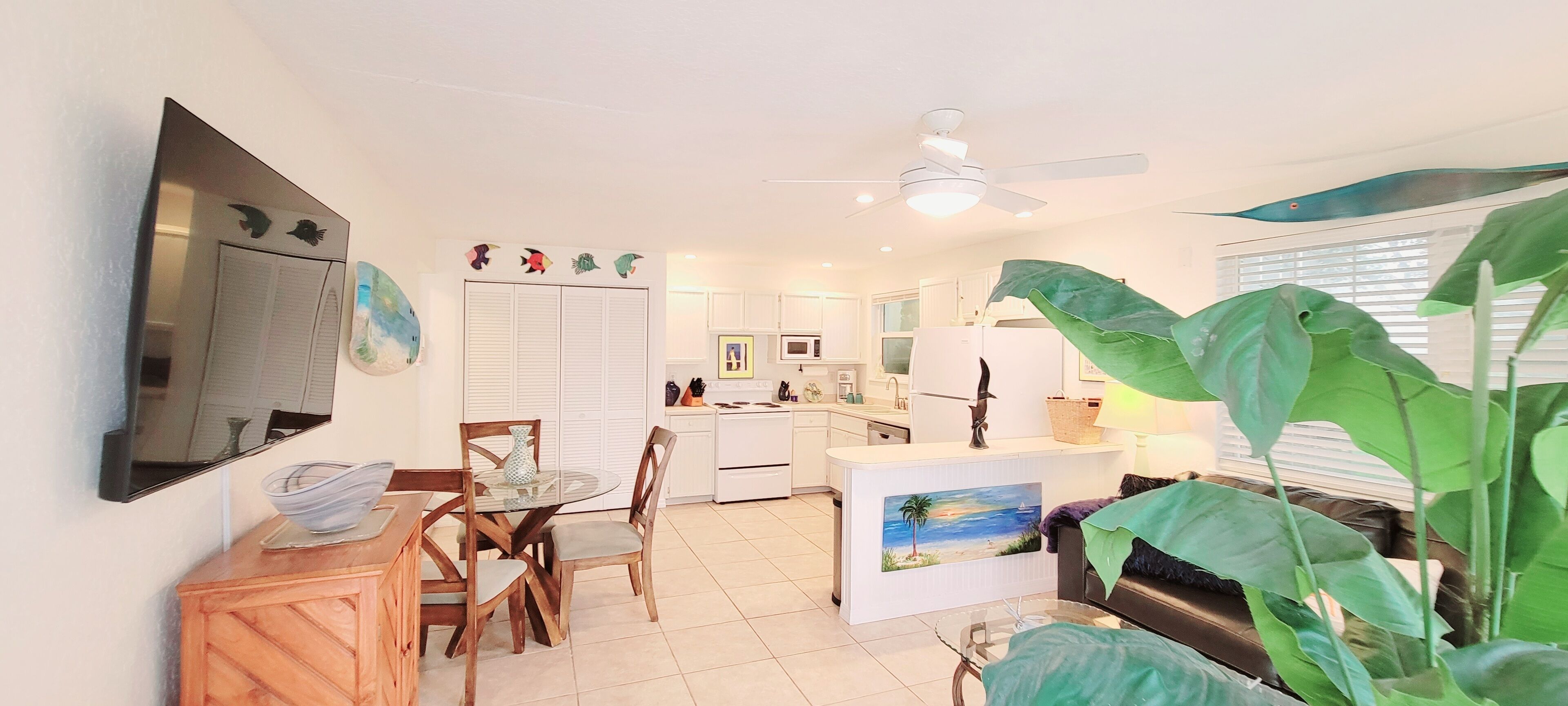 A modern kitchen with white cabinets, a microwave, and a sink. There is a dining area with a glass table and chairs.