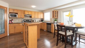 A modern kitchen with wooden cabinets, a central island, and a dining area with chairs. - Marvelous  Bedroom House on Comdale (Winnipeg)