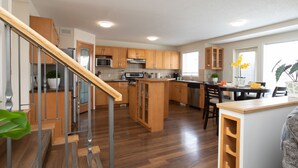 A modern kitchen with wooden cabinets, a central island, and a dining area with chairs. - Marvelous  Bedroom House on Comdale (Winnipeg)