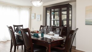 A dining room with a wooden table set for six, surrounded by chairs. A dark wooden cabinet with glass doors is against the wall. - Marvelous  Bedroom House on Comdale (Winnipeg)