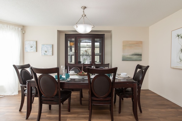 A dining room with a wooden table and chairs, a chandelier, and framed artwork on the walls.
