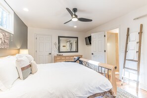 A bedroom with a bed, a ceiling fan, a dresser, a mirror, and a TV mounted on the wall.
