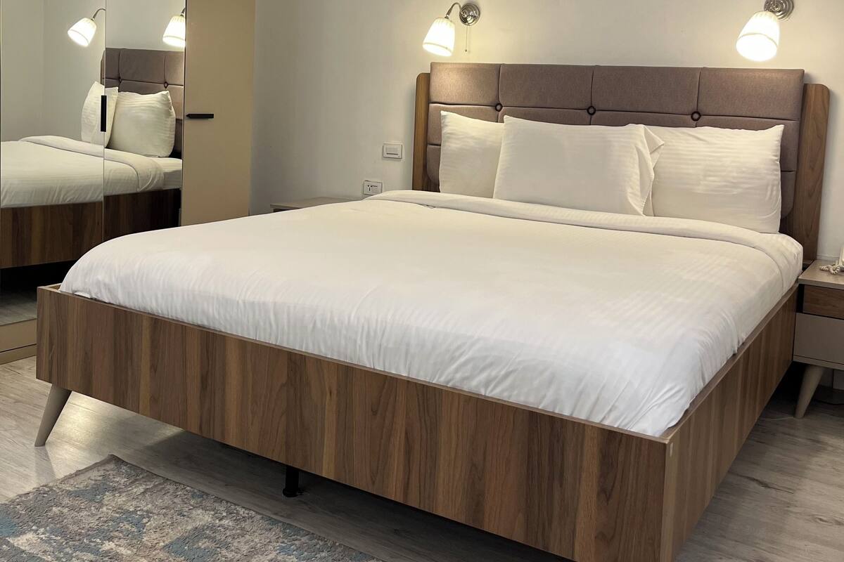 A bedroom with a large bed, wooden headboard, bedside lamps, and a mirror.