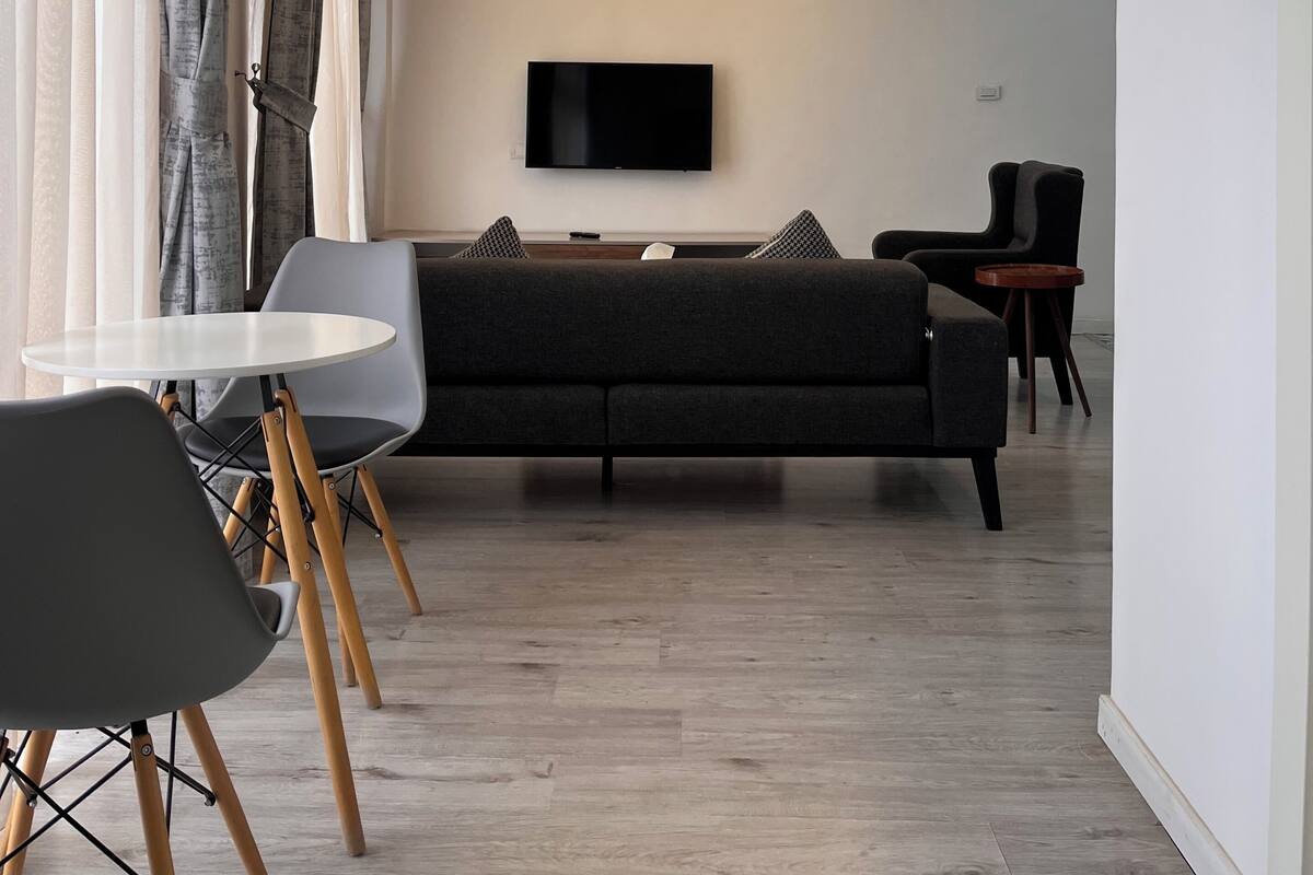 A modern living room with a sofa, a TV, and a dining area with chairs and a table.