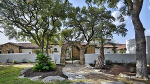 A courtyard with a stone archway, large trees, and a well-maintained garden. - Boerne Hacienda with Pool and Spa (Boerne)