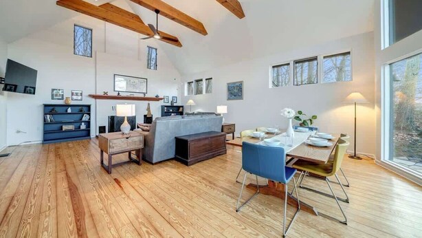 A spacious living area with a dining table, blue chairs, and a wooden floor. - Exclusive Wooded Chalet w Magnificent River Views (Shepherdstown)