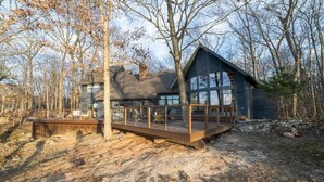 Eine Hütte mit Terrasse und großen Fenstern, umgeben von Bäumen.