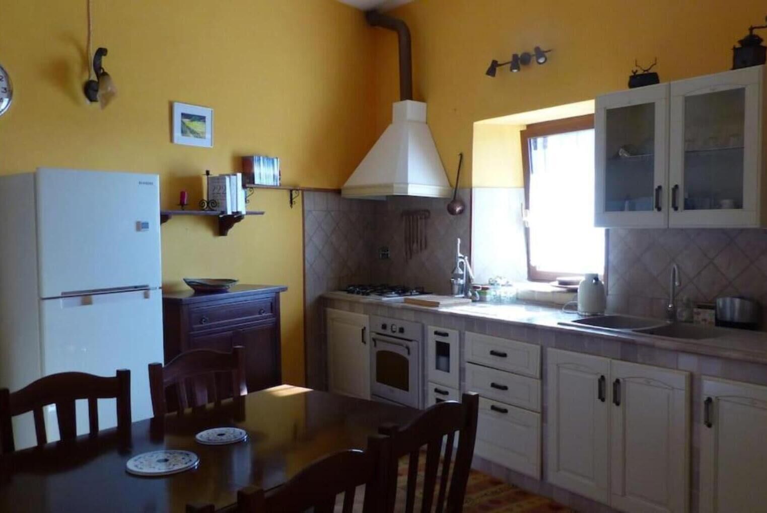 Una cocina con estufa, pileta, armarios y una mesa de comedor con sillas.