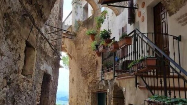 A narrow cobblestone street flanked by stone buildings with arched doorways and balconies. - Casa Romantica in un Borgo Antico in Sabina (Cicignano)