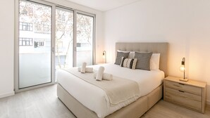 A modern bedroom with a large bed, a nightstand, and a sliding glass door leading to a balcony.