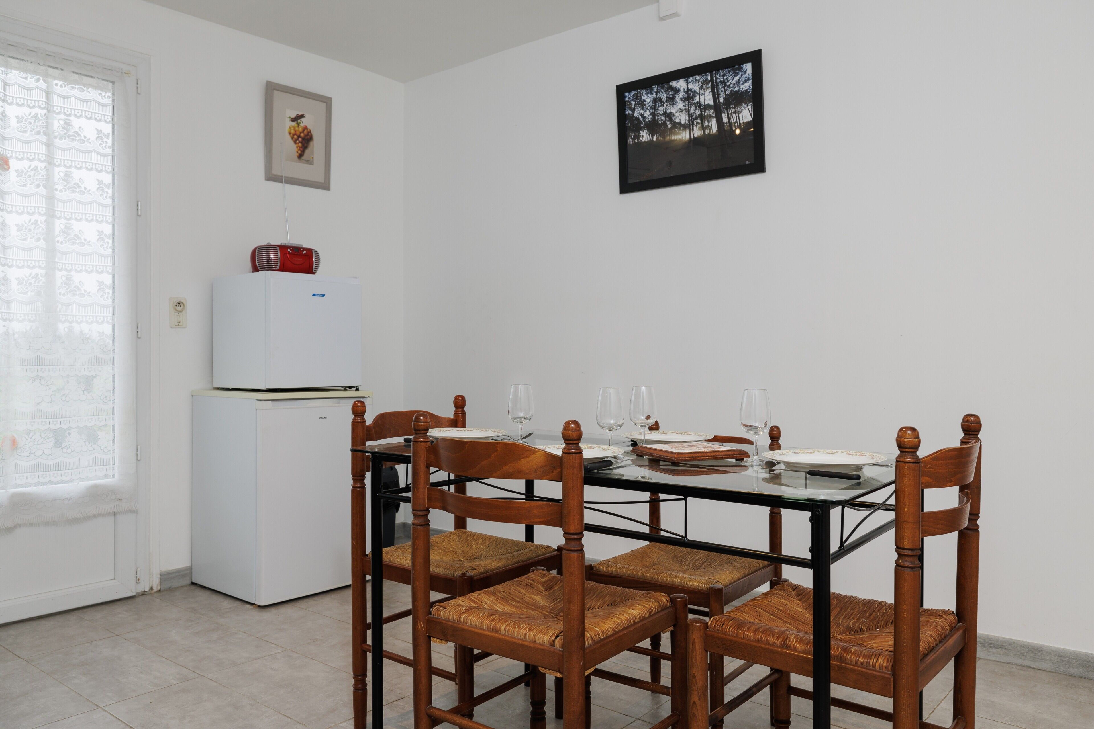 A dining area with a glass table, wooden chairs, a white refrigerator, and a framed picture on the wall.