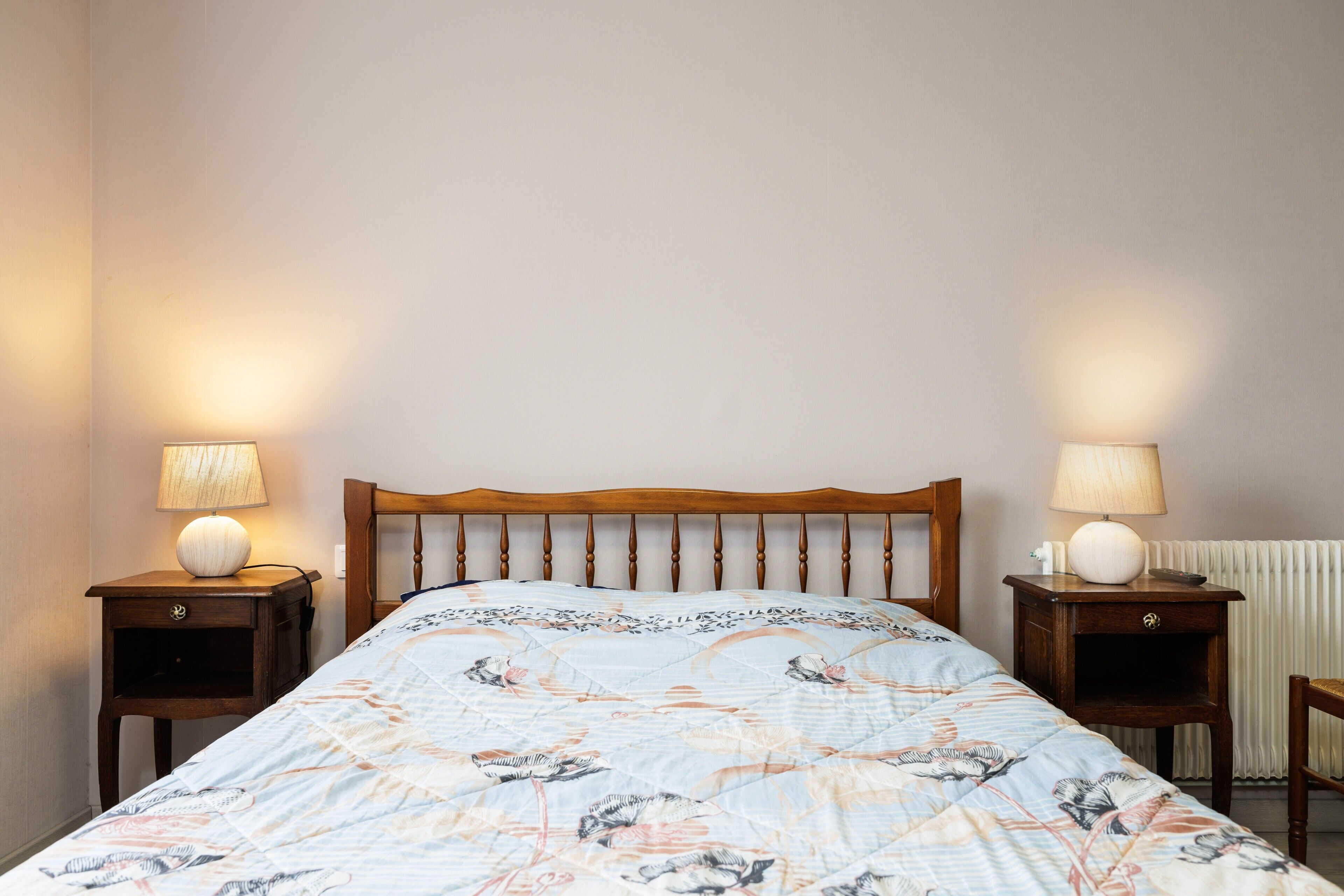 A bedroom with a wooden headboard, two bedside tables with lamps, and a floral-patterned bedspread.