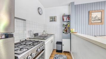Une cuisine de taille réduite avec des meubles blancs, une cuisinière à gaz, un évier et une horloge au mur.