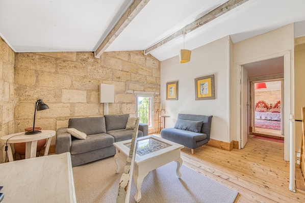 A living room with stone walls, two grey sofas, a white coffee table, and a wooden floor.